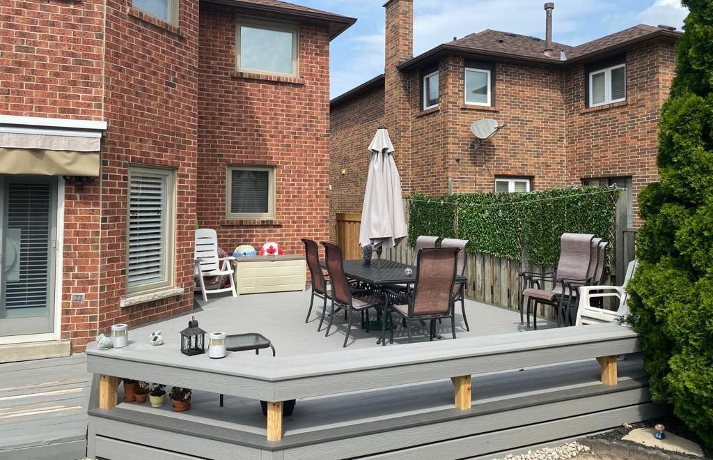 A patio with a table and chairs and an umbrella in front of a brick house.