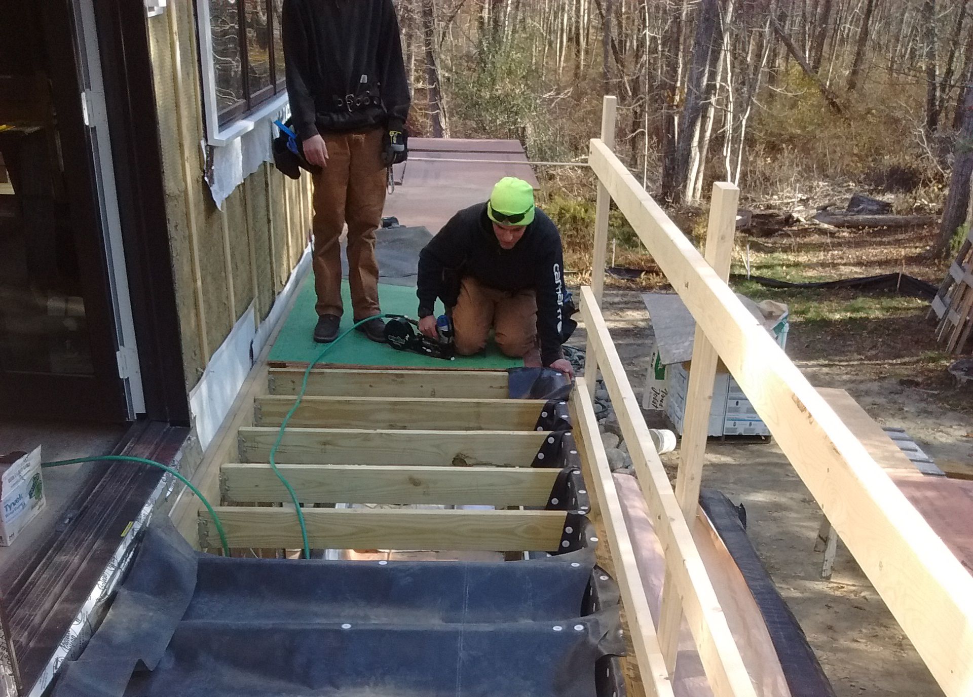 Two men are working on a wooden deck in the woods