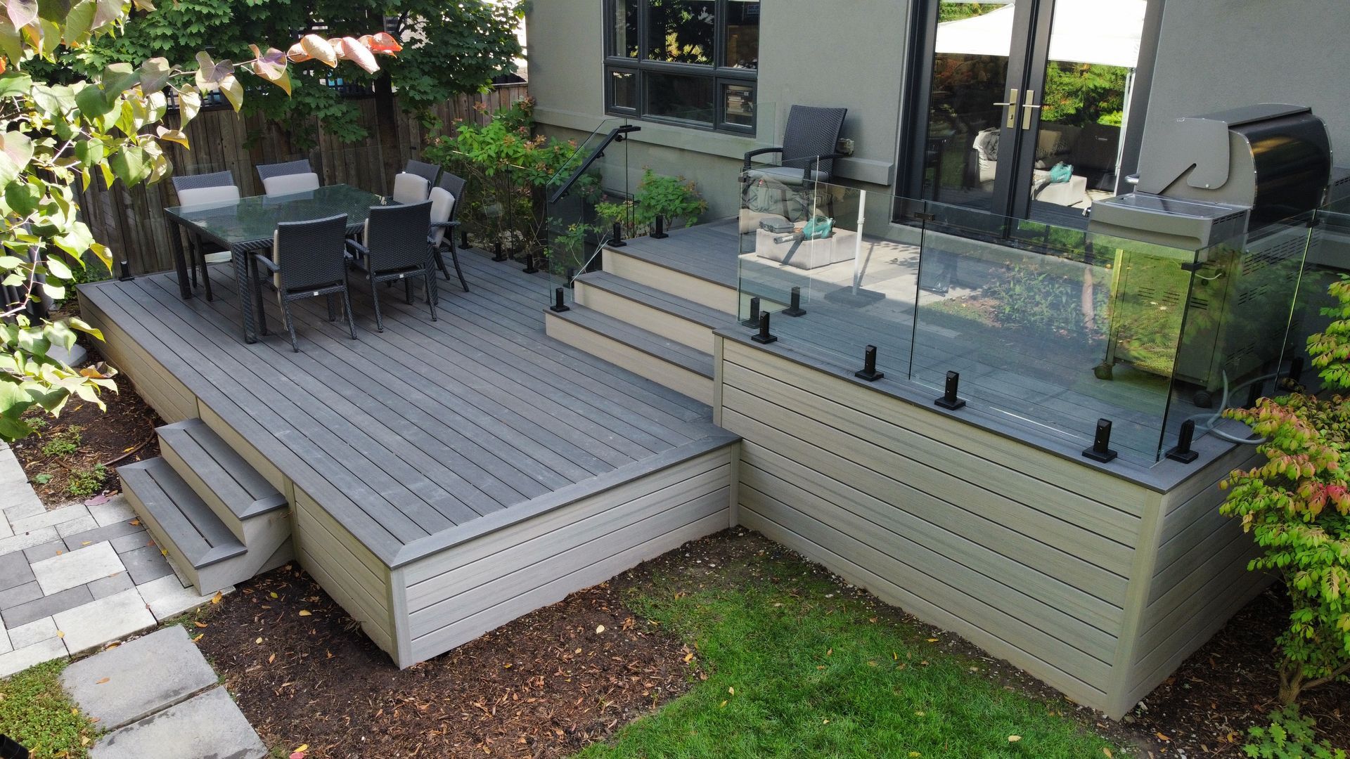 Split-level gray deck with glass railings and outdoor dining area.