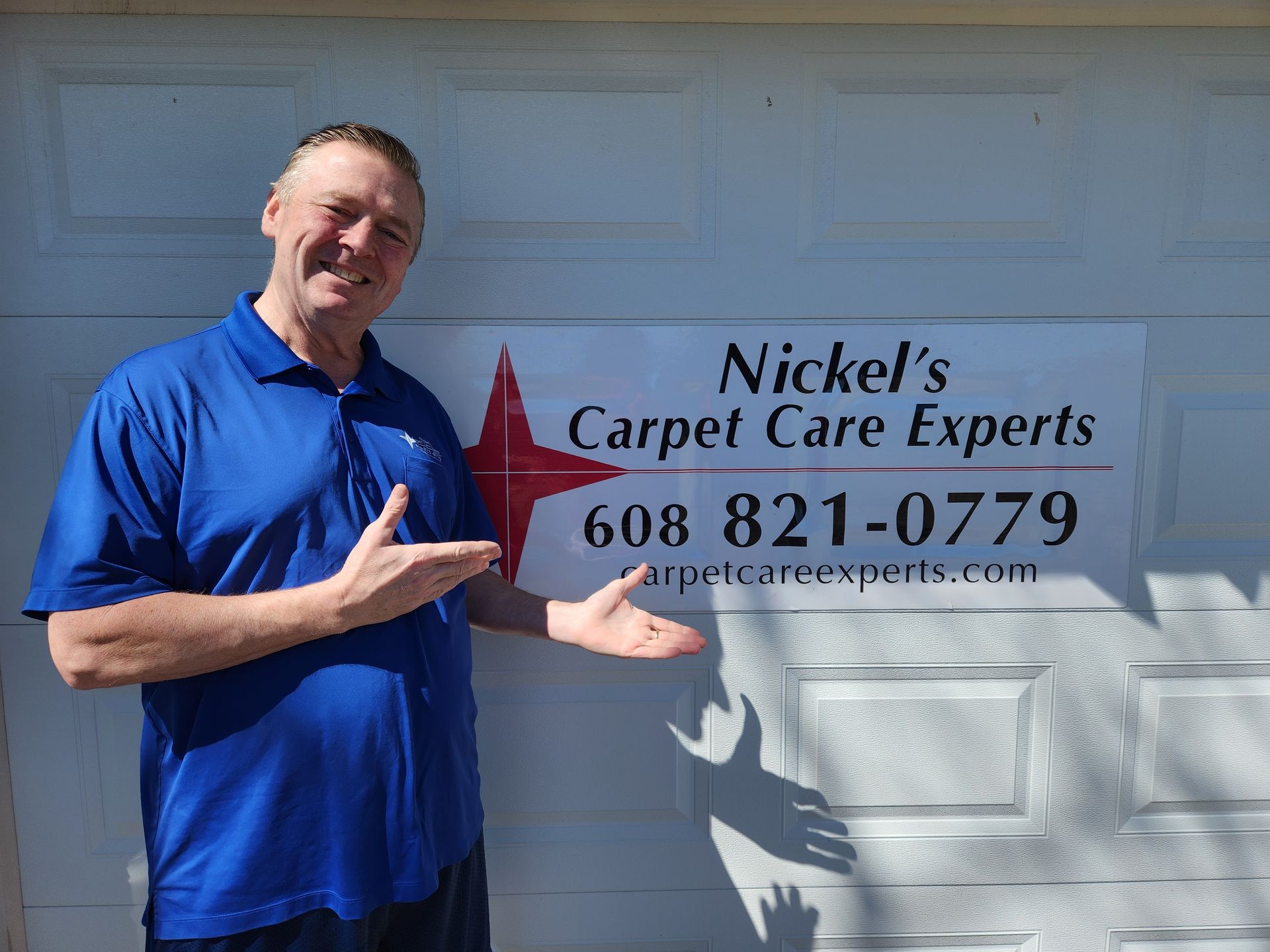 A man in a blue shirt is standing in front of a sign for nickel 's carpet care experts