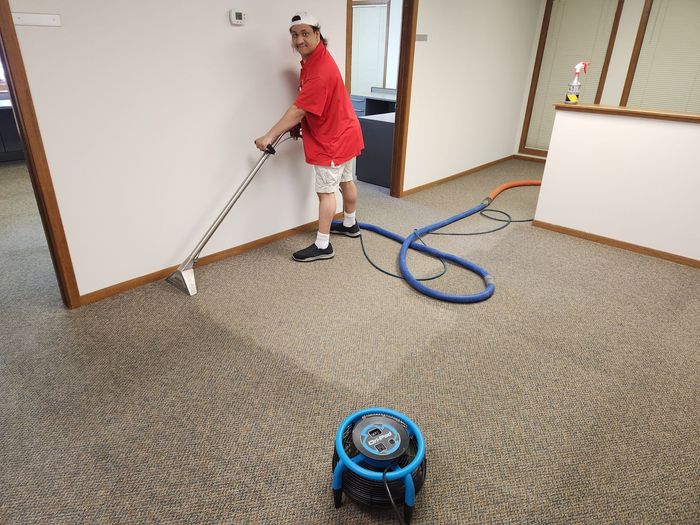 A man is cleaning a carpet with a vacuum cleaner.