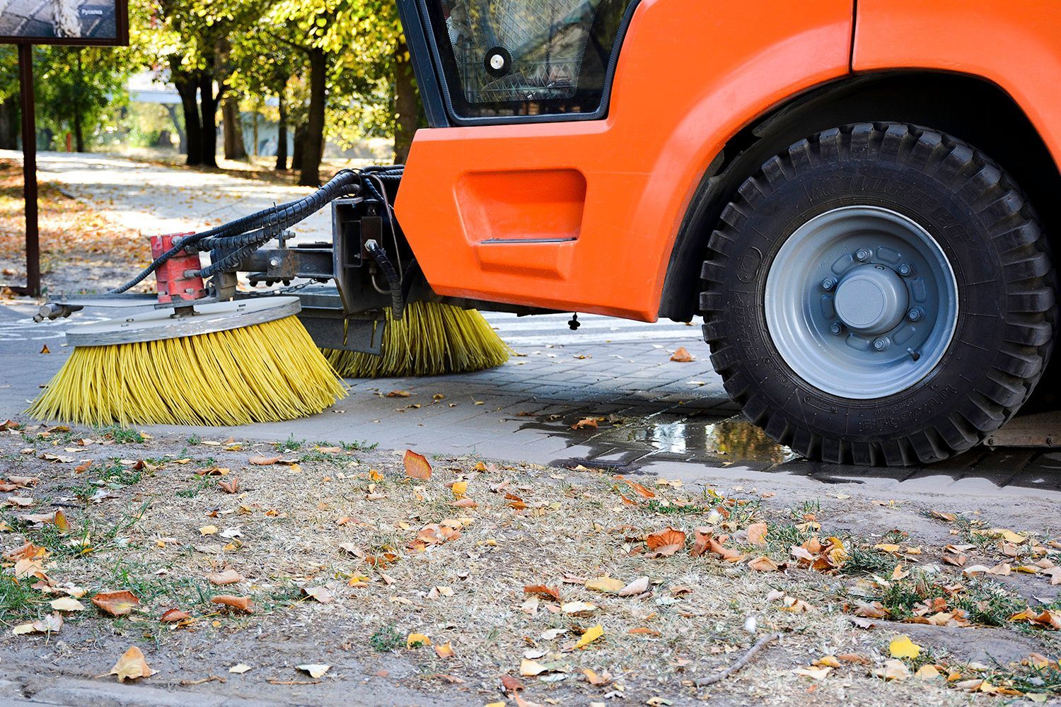 Orange street sweeper with yellow brushes cleaning leaves on pavement. Orange street sweeper with yellow brushes cleaning leaves on pavement.
