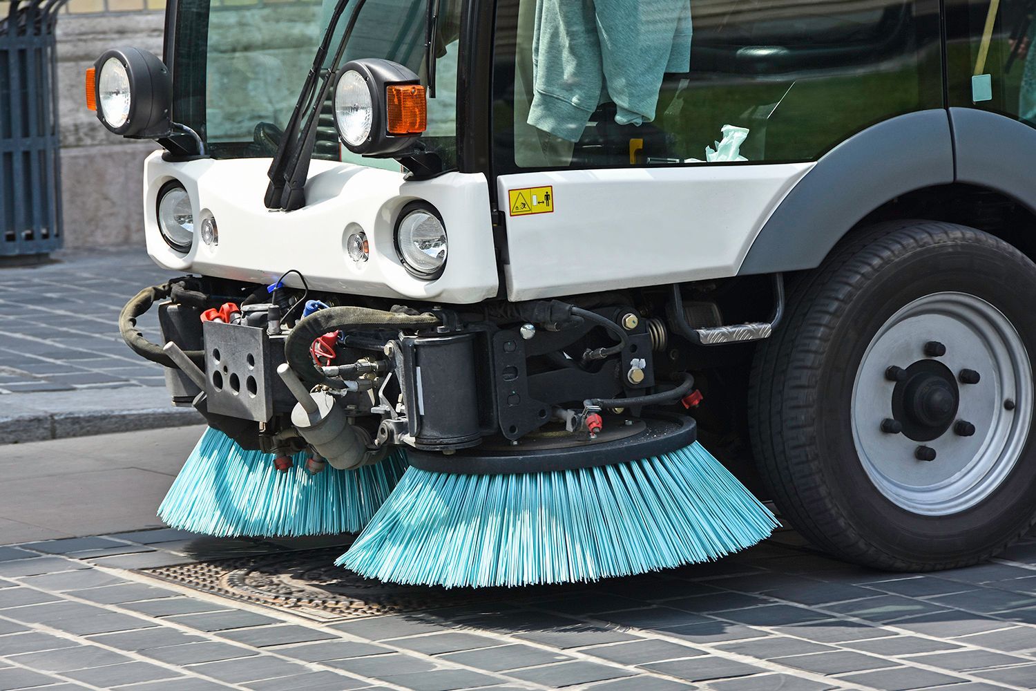 Street sweeper with blue brushes cleaning a brick road.