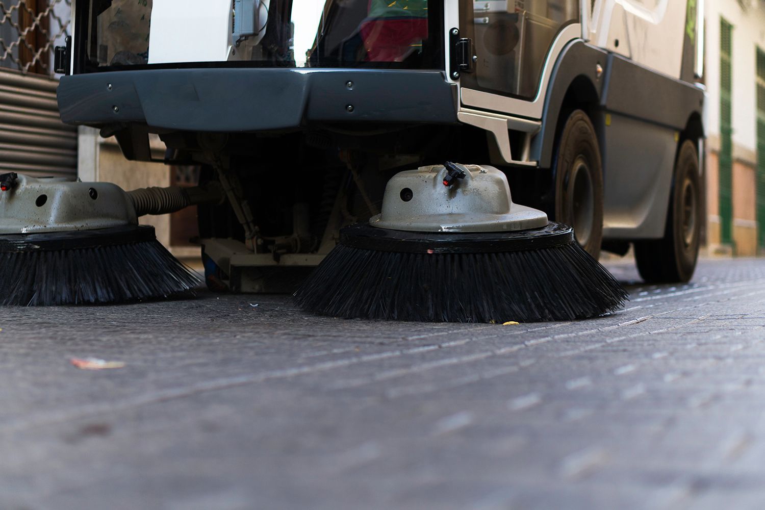 Street sweeper with brushes sweeping a cobblestone street.