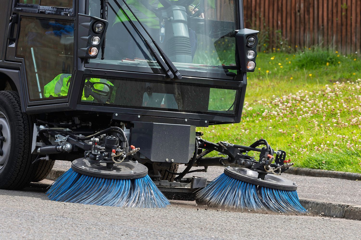 Street sweeper with blue brushes cleaning a paved road.