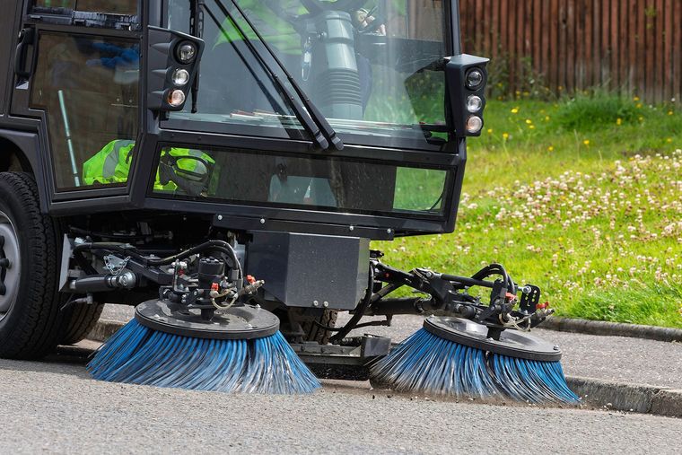 Street sweeper with blue brushes cleaning a paved road.