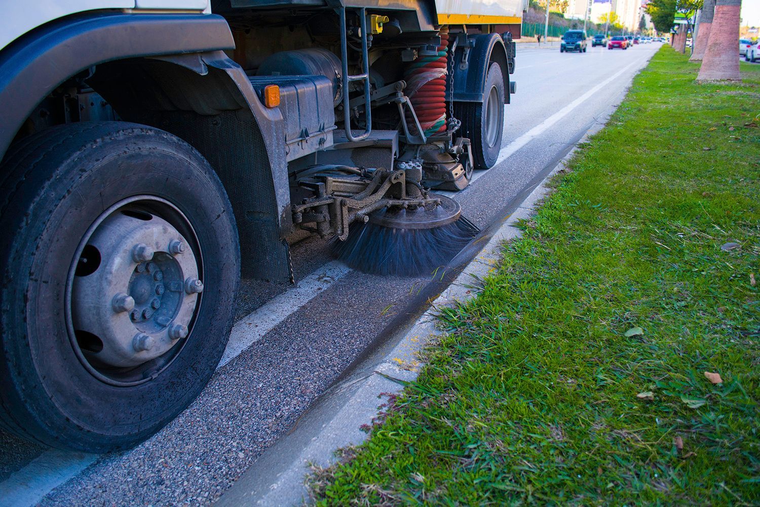 Street sweeper cleaning the curb of a road with green grass on the right.