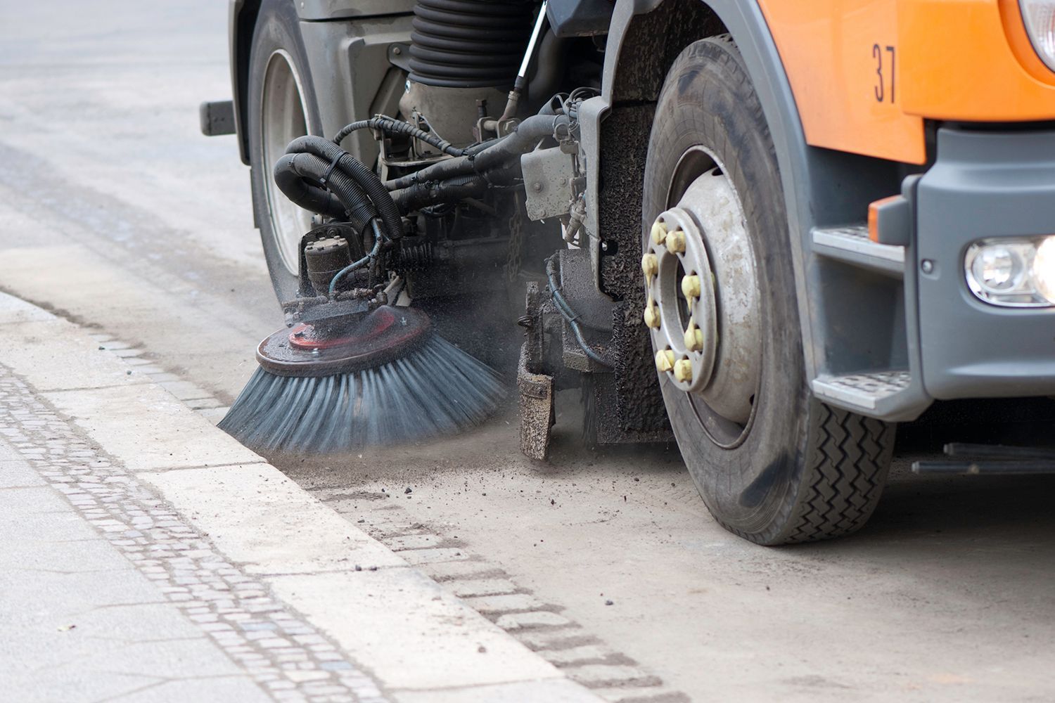 Street sweeper cleaning a sidewalk. Orange truck with large brush sweeping dirt. Street sweeper cleaning a sidewalk. Orange truck with large brush sweeping dirt.