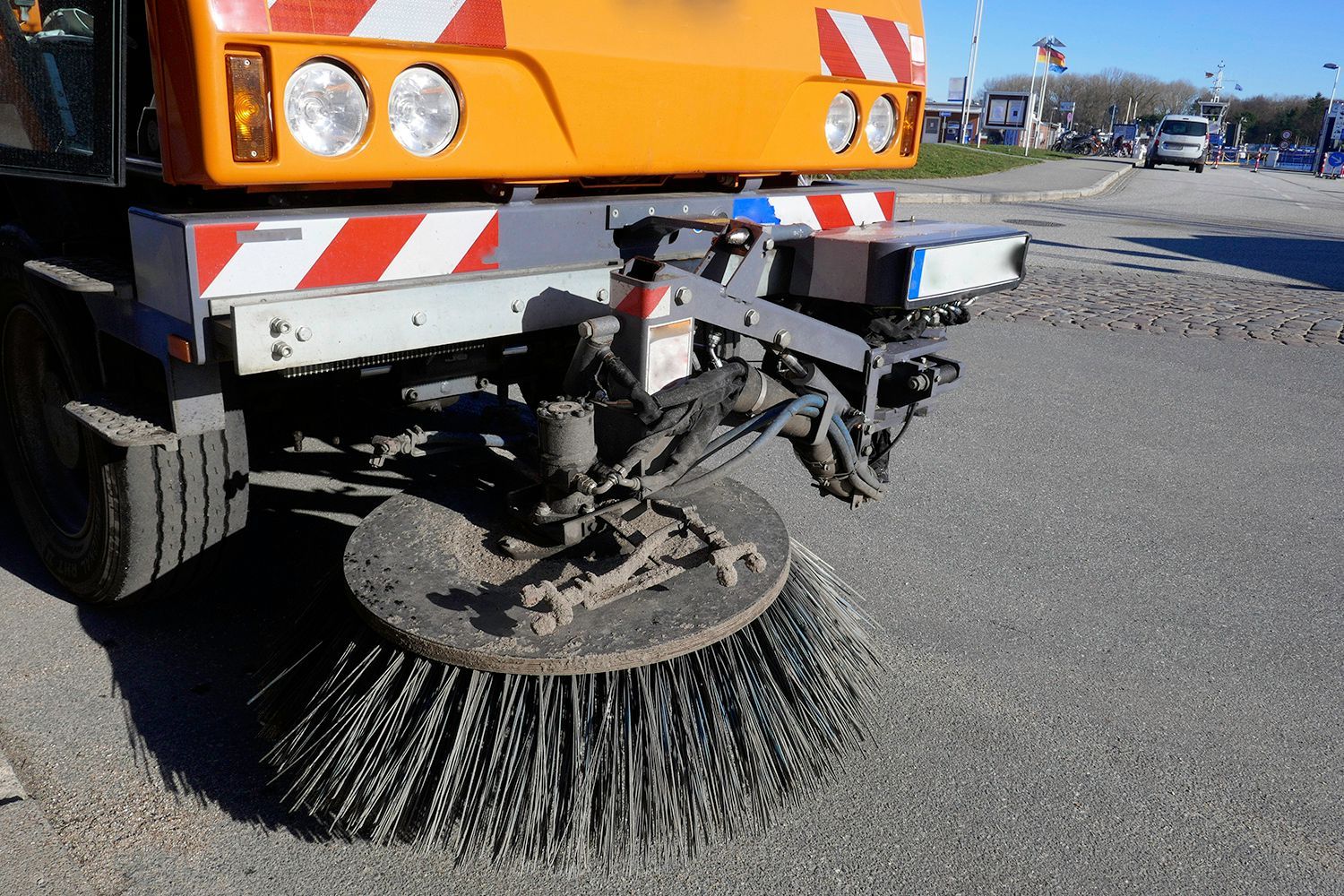 Orange street sweeper, front detail, sweeping asphalt, outdoor.