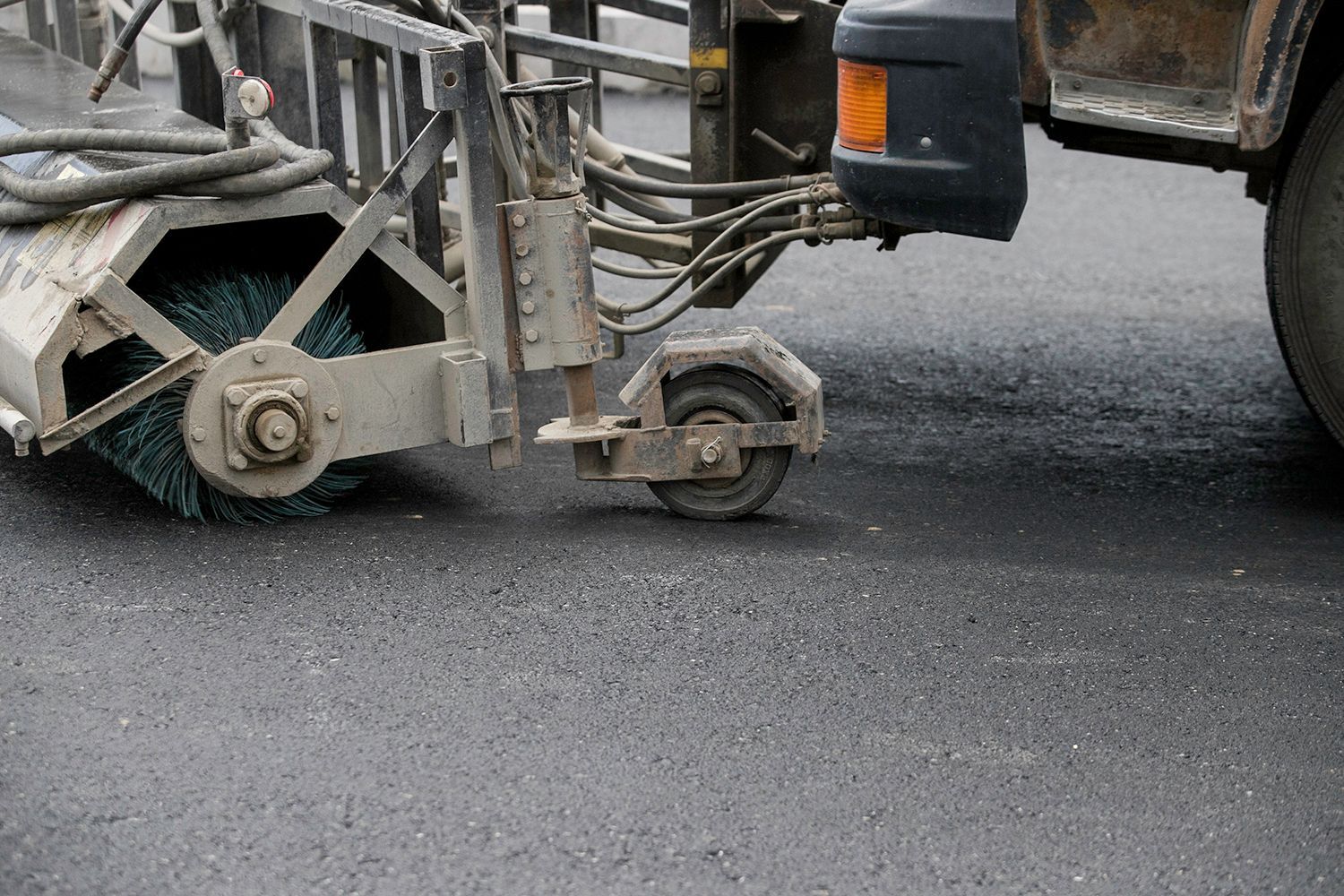 Street sweeper cleaning freshly paved asphalt road.