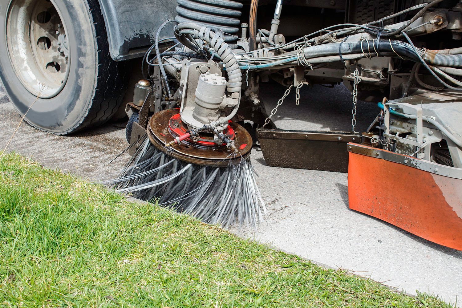 Street sweeper cleans the curb, with rotating brush sweeping debris off the asphalt.