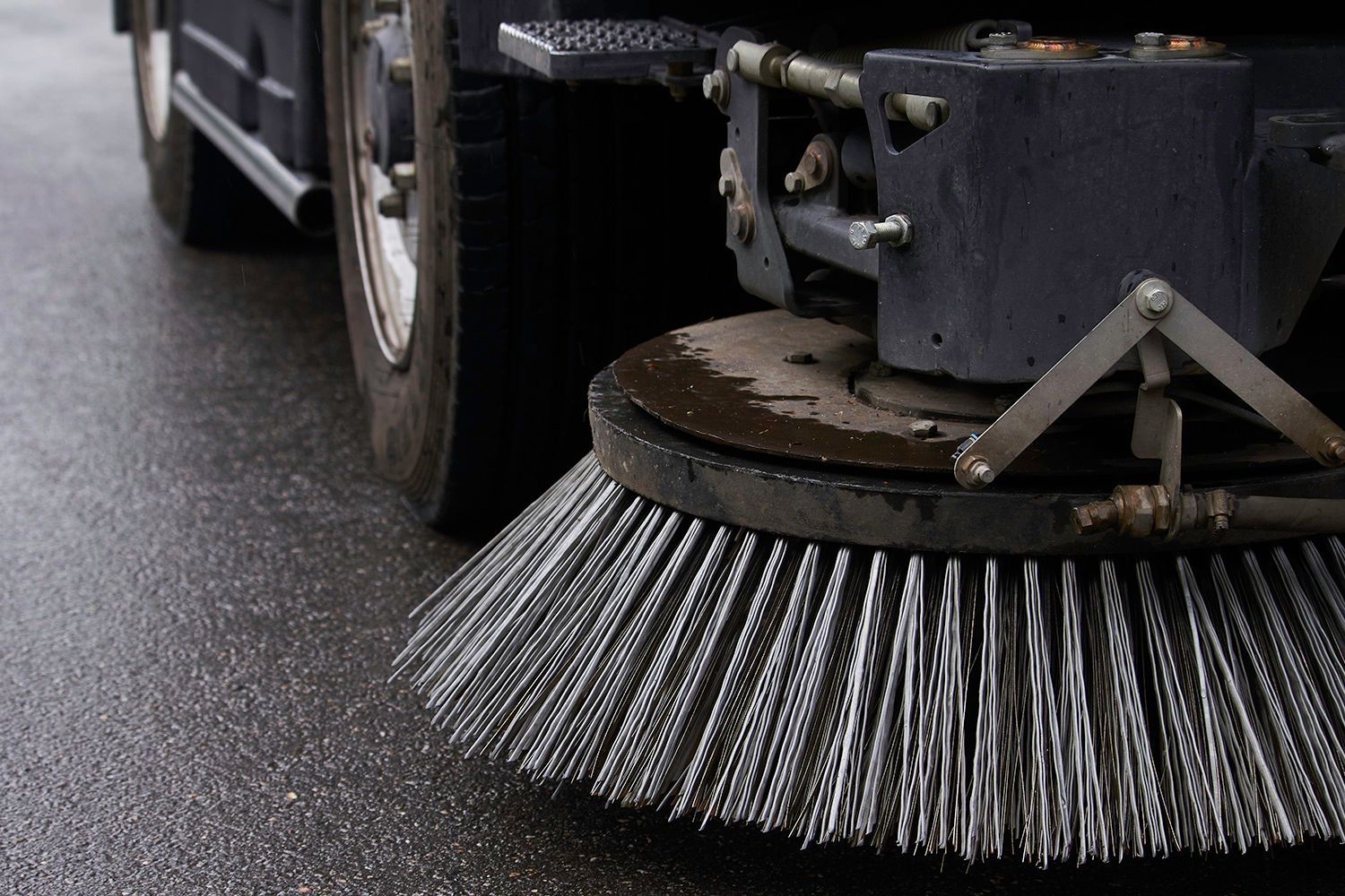 Street sweeper brush sweeping wet asphalt, close-up view. Street sweeper brush sweeping wet asphalt, close-up view.