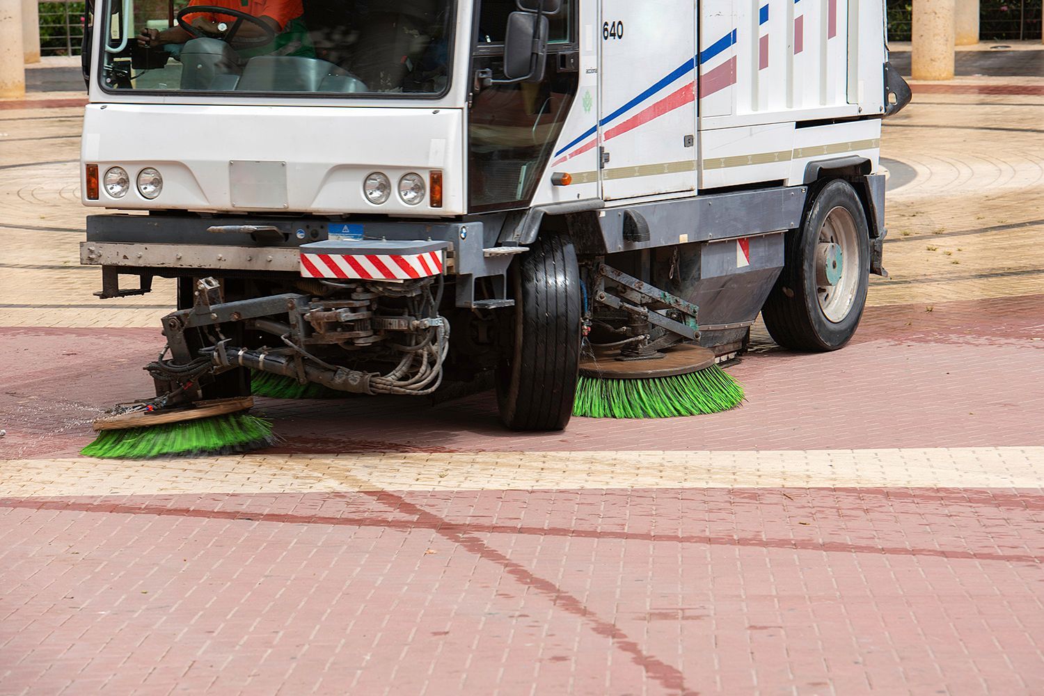 Street sweeper cleaning a red brick paved area. White truck with green brushes in action. Street sweeper cleaning a red brick paved area. White truck with green brushes in action.