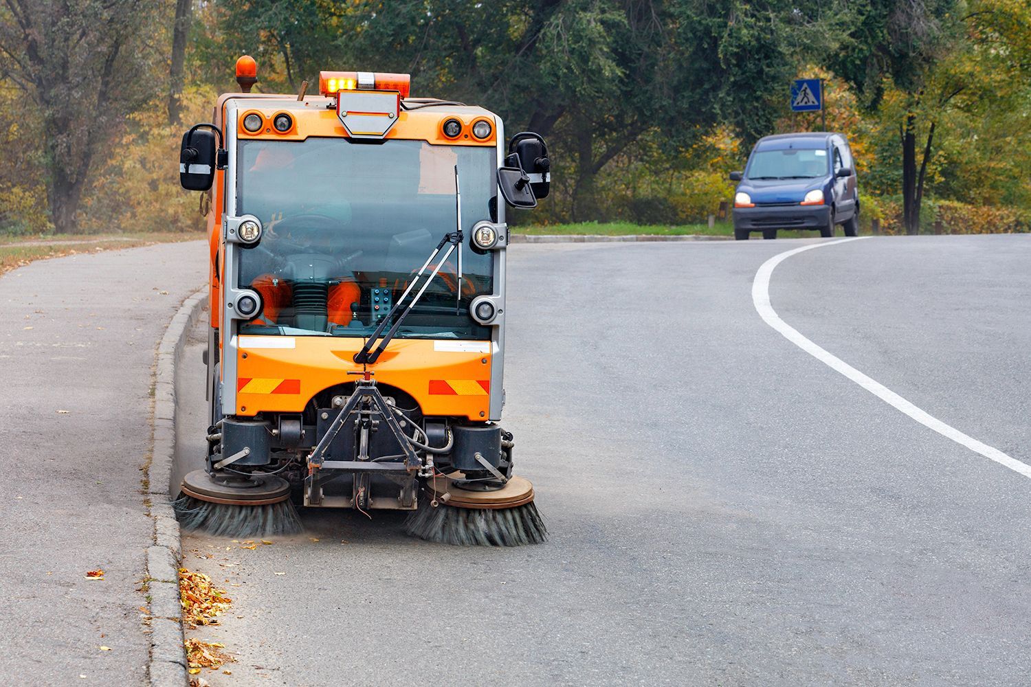 Street sweeper cleaning road. Orange and gray vehicle. Car in background.