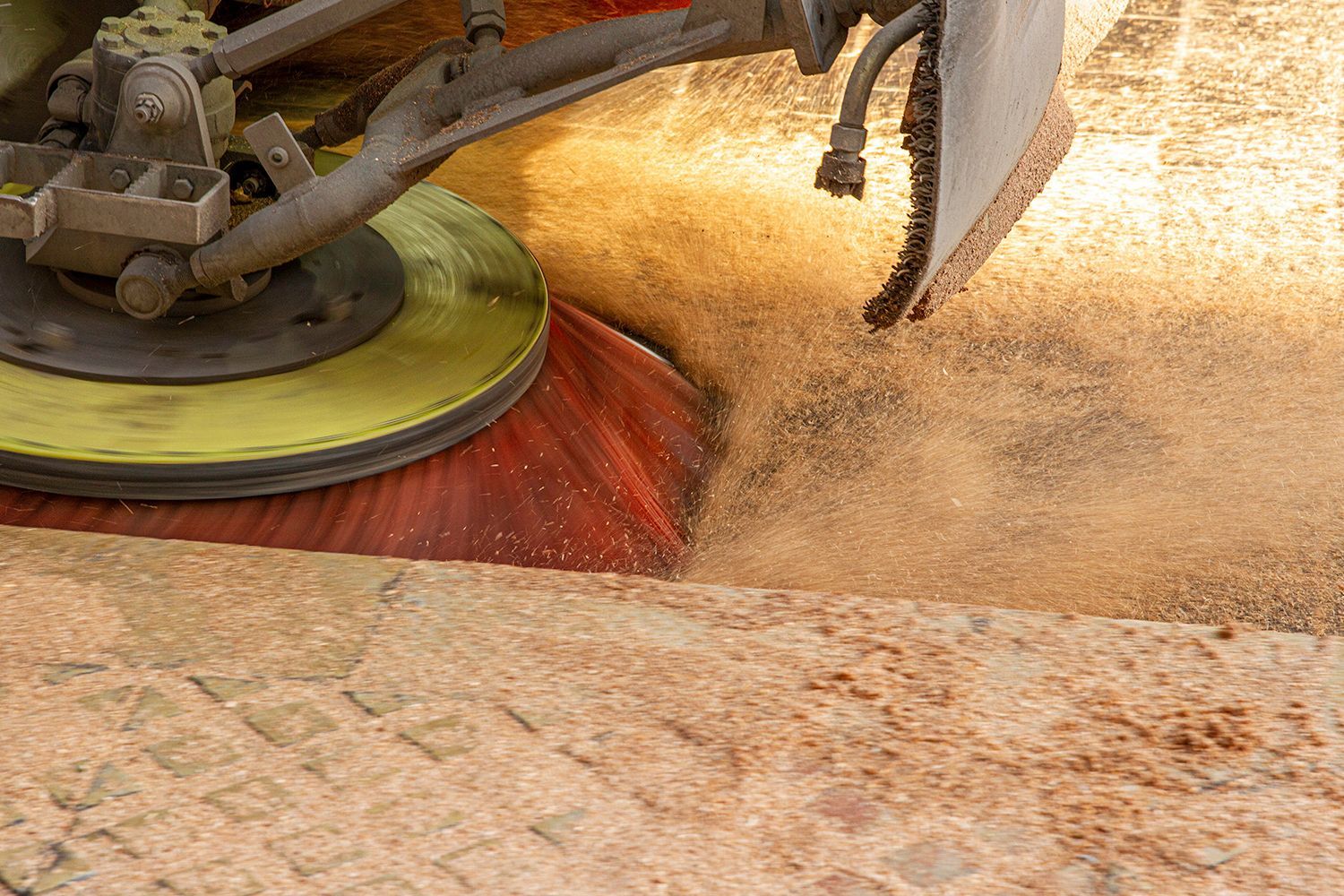 Street sweeper cleaning a cobblestone street, kicking up dust with its rotating brushes.