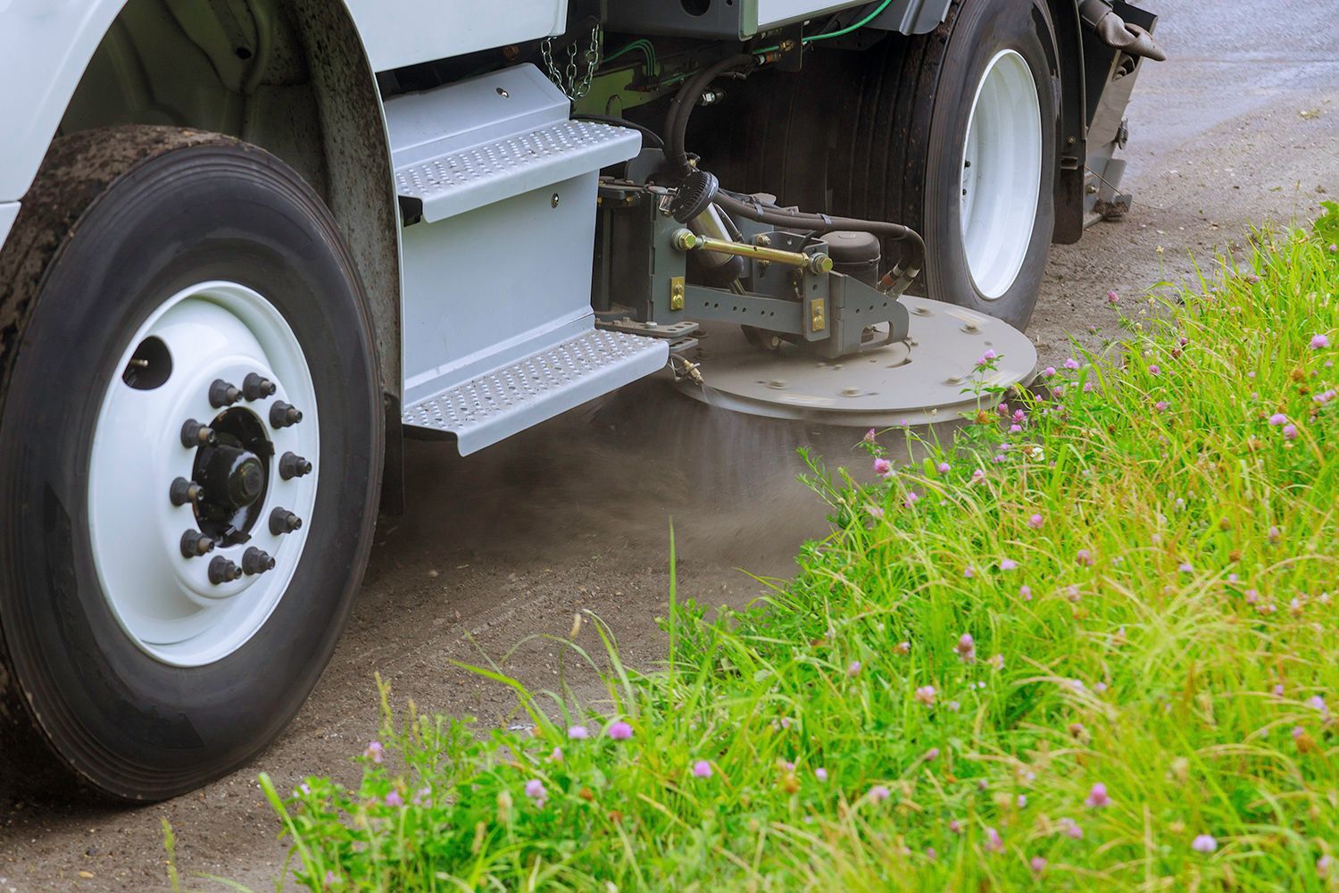 Street sweeper spraying the edge of a road lined with green grass. Street sweeper spraying the edge of a road lined with green grass.