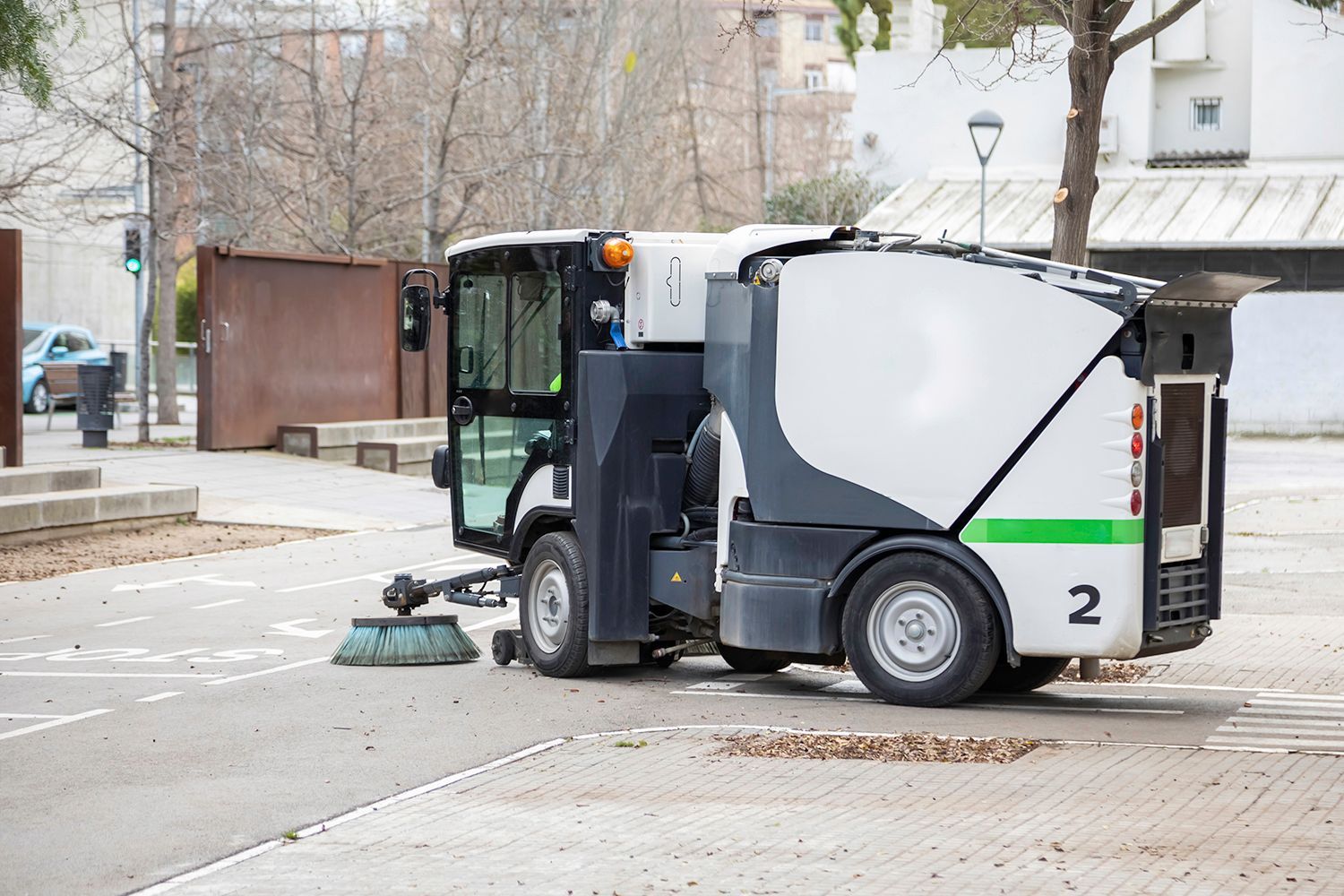 Street sweeper cleaning an asphalt road in a public space. White and gray vehicle, brush sweeping. Street sweeper cleaning an asphalt road in a public space. White and gray vehicle, brush sweeping.