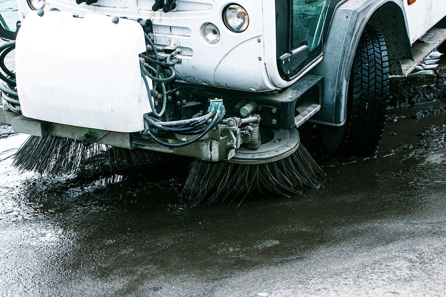 Road sweeper with rotating brushes cleaning a wet street.