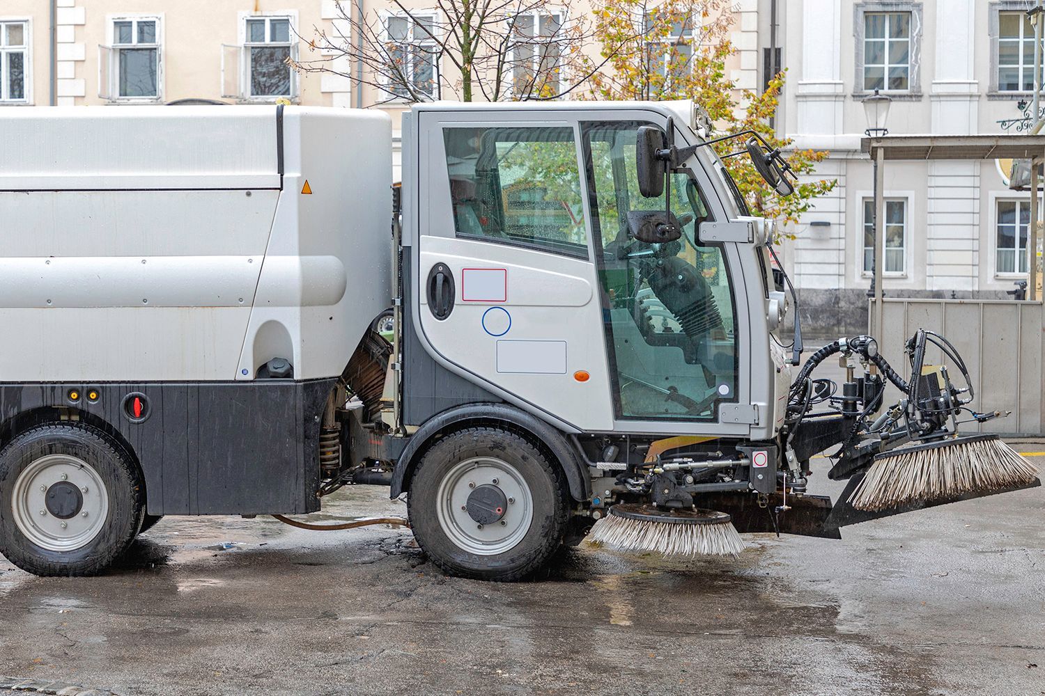 White street sweeper truck cleaning a wet street in front of a building.