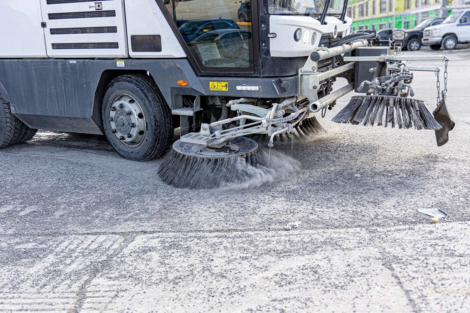 Street sweeper cleaning a snow-covered road with rotating brushes in a city setting. Street sweeper cleaning a snow-covered road with rotating brushes in a city setting.