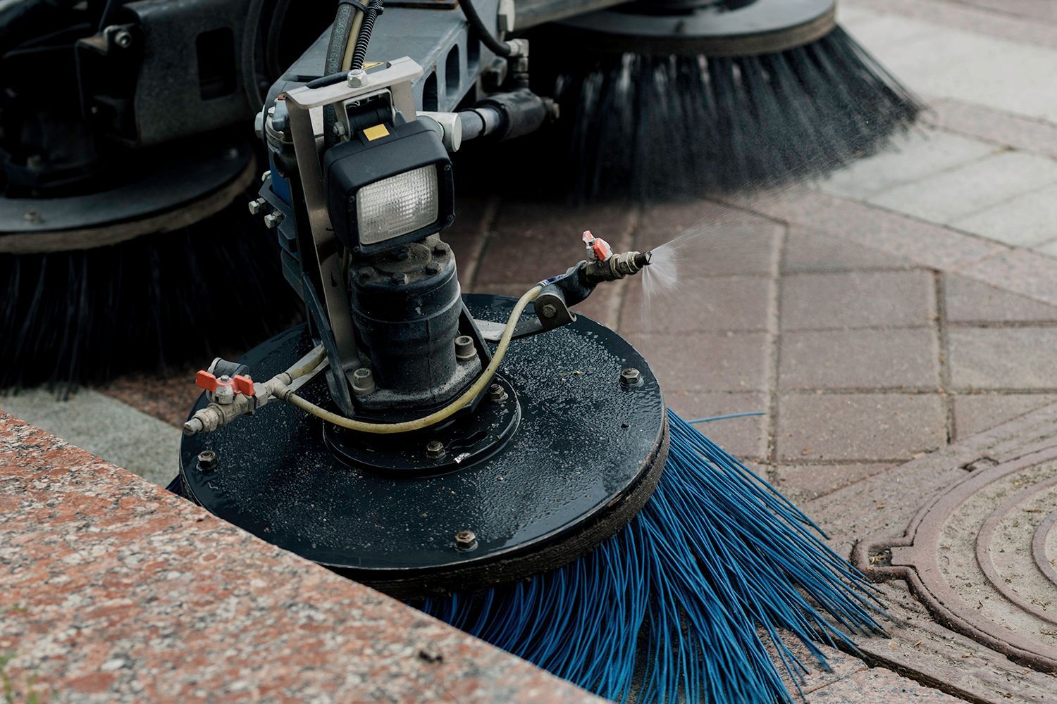 Street sweeper with blue brushes cleaning a tiled sidewalk. Street sweeper with blue brushes cleaning a tiled sidewalk.