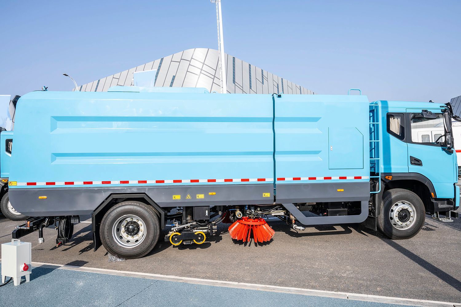 Blue street sweeper truck on pavement, red brush visible. Blue street sweeper truck on pavement, red brush visible.