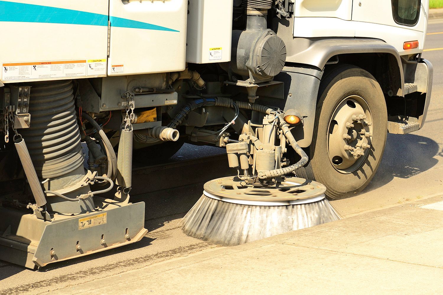 Street sweeper truck brushes sweeping a road. Gray asphalt.