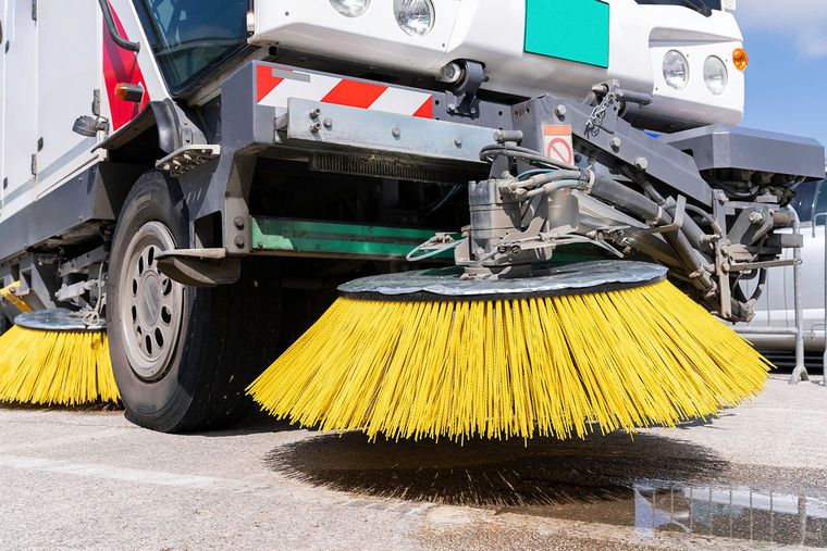 Street sweeper with yellow brushes cleaning a paved surface.