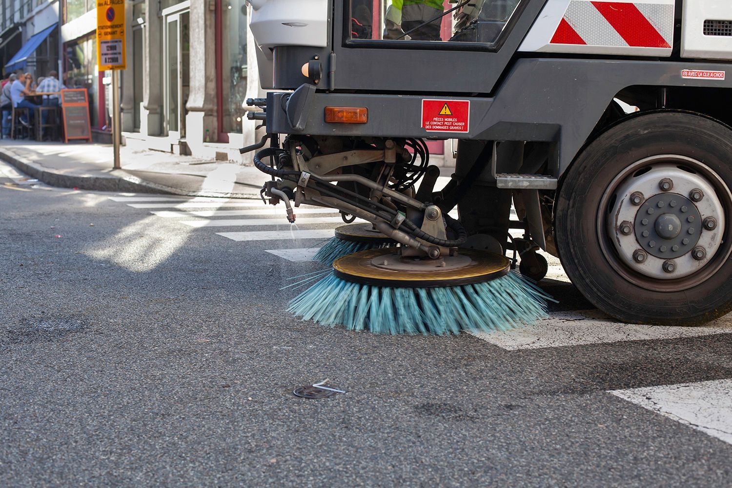 Street sweeper with blue brushes cleaning a paved street.