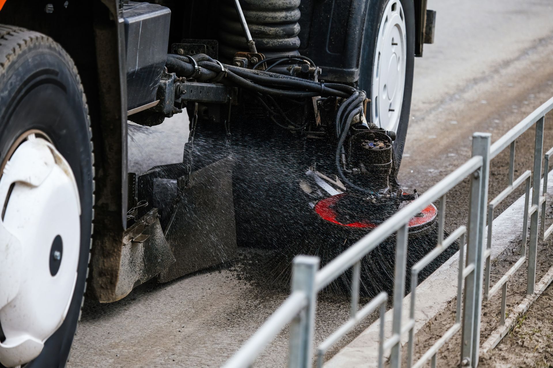 Road sweeper brushes cleaning a pedestrian crosswalk, kicking up dust. Vehicle sweeping streets, cleaning up sidewalk