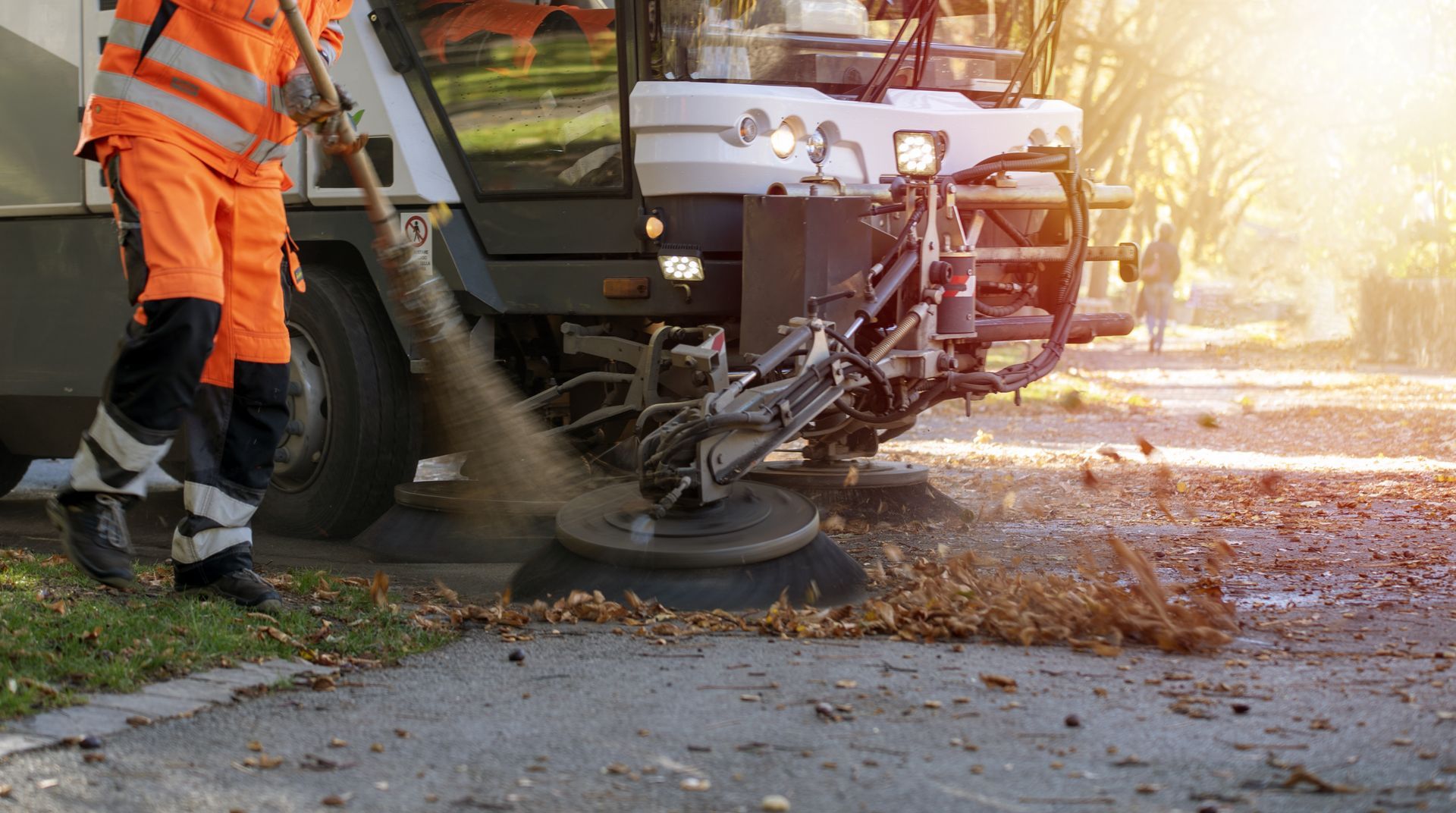 A street sweeper machine cleaning leaves from a roadside