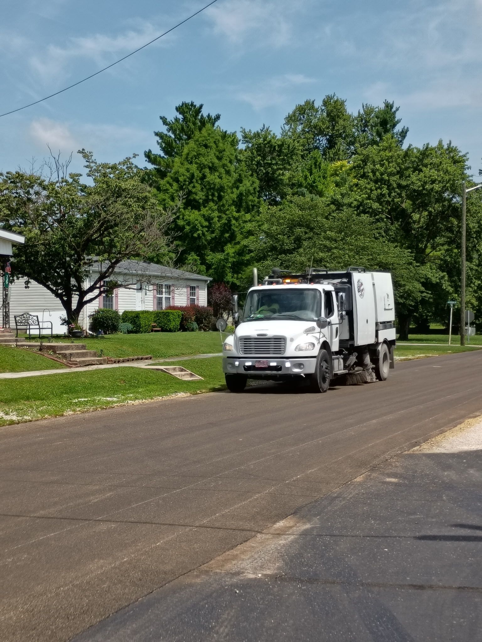 Street sweeper cleaning the curb of a road with green grass on the right.