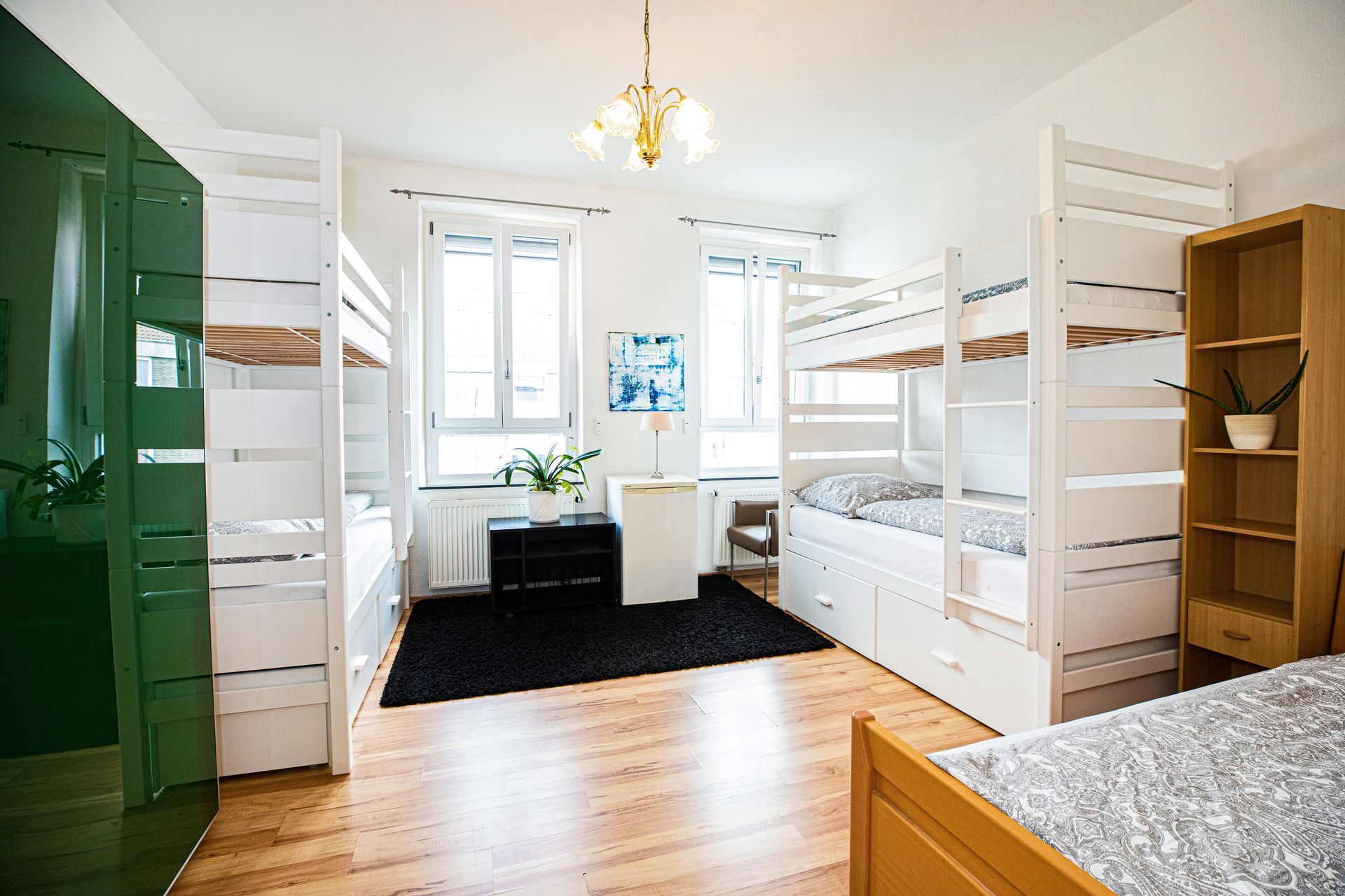 A bright hostel room with bunk beds, wooden floors, and a black rug.