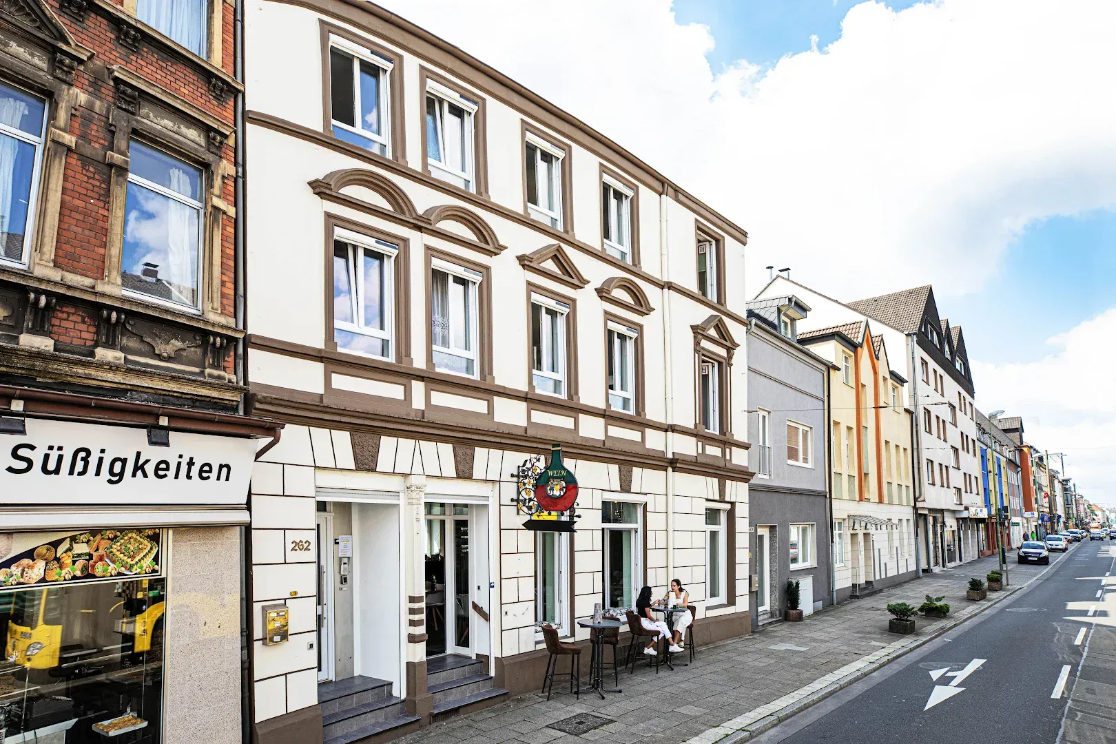 Street view of European buildings, including a restaurant with outdoor seating and the word