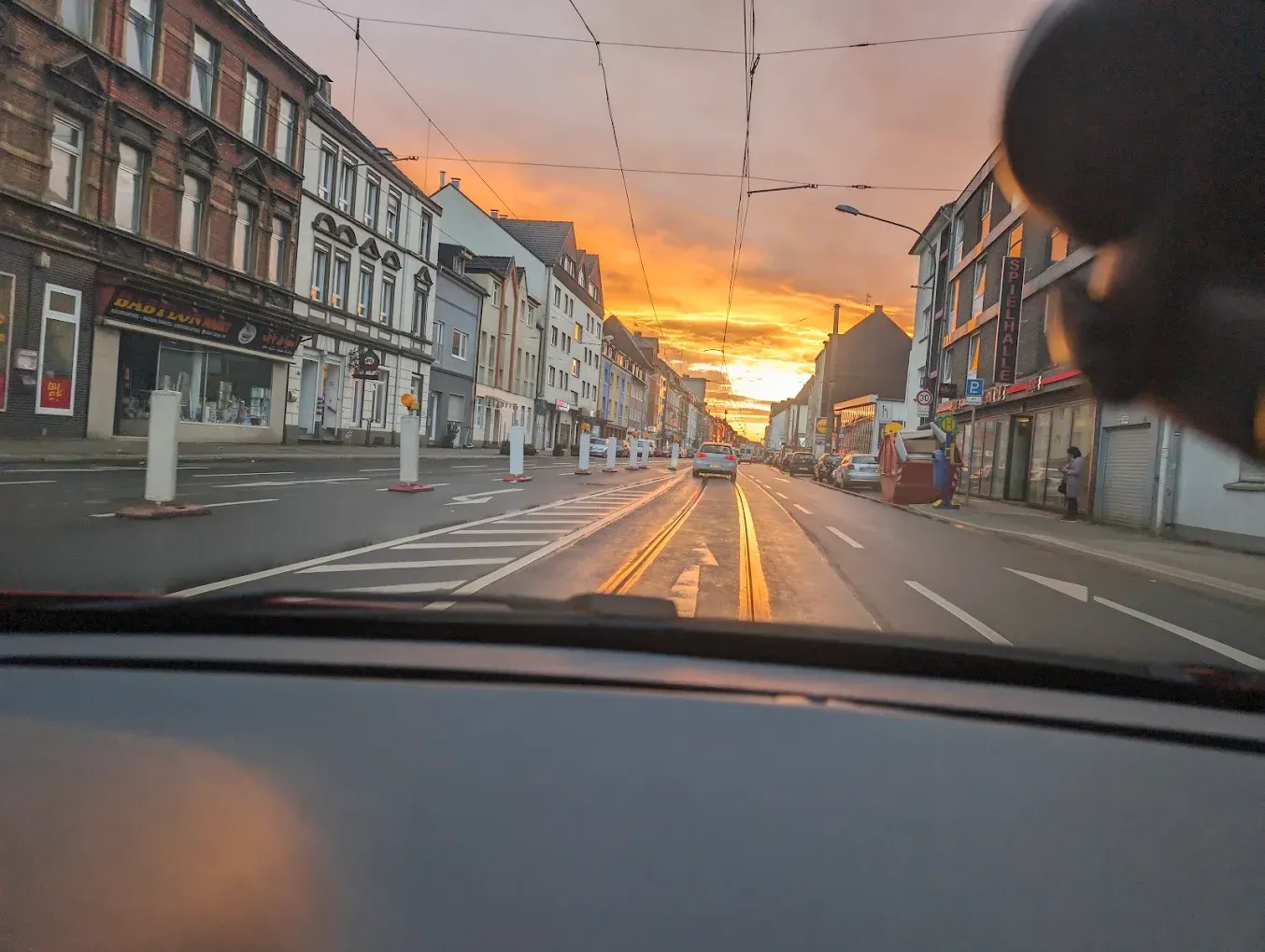 View from a car driving down a city street at sunset. Buildings line the road with golden light reflecting on wet pavement.