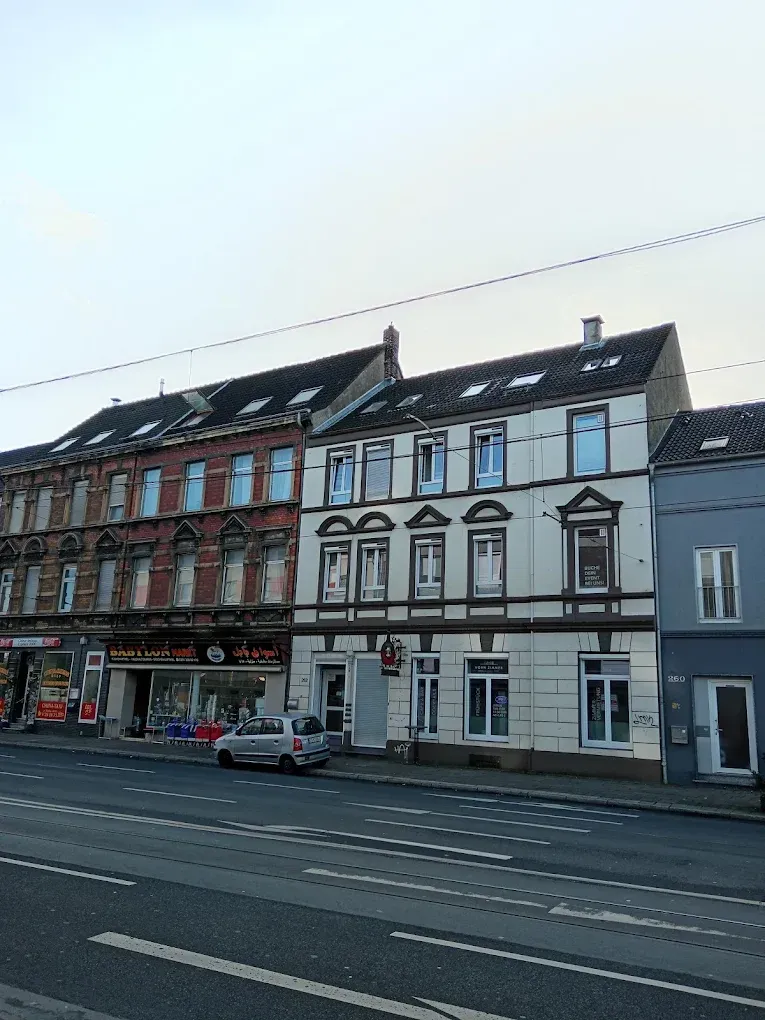 Buildings along a street, white and red facades. A car is parked in front.