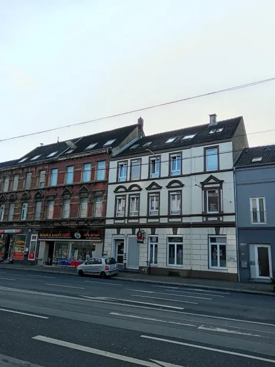 Buildings along a street, white and red facades. A car is parked in front.