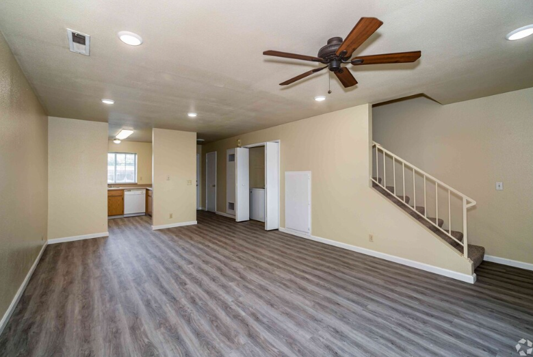 An empty living room with a ceiling fan and stairs.