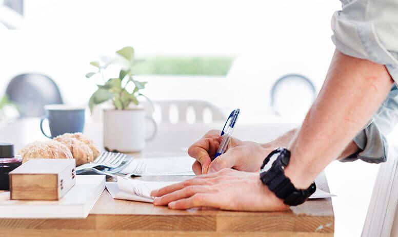 A man is sitting at a table writing on a piece of paper.