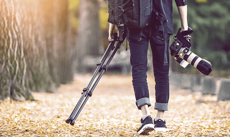 A photographer is walking down a path holding a camera and a tripod.