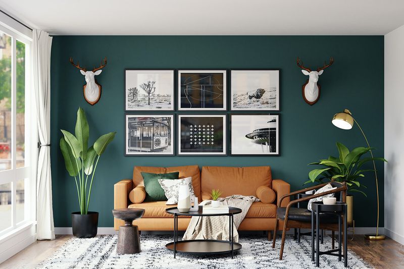 A living room with green walls , a brown couch , a coffee table , and a deer head on the wall.