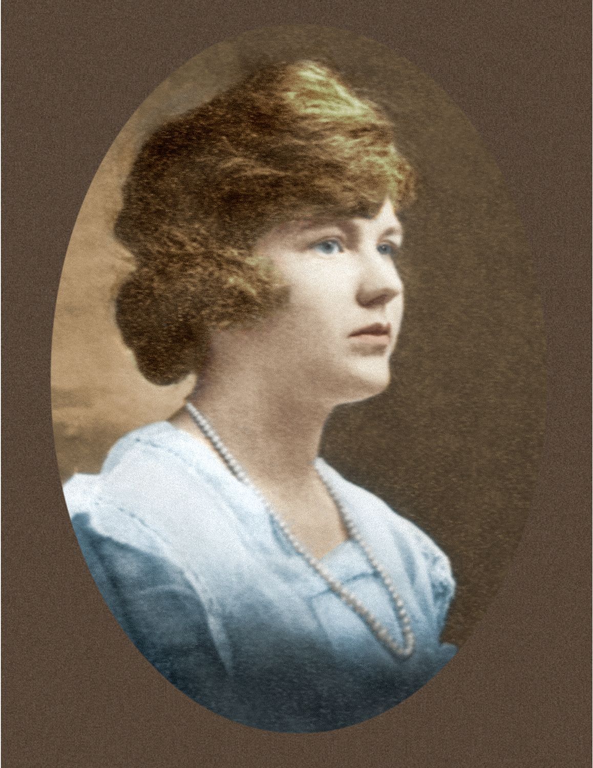 A black and white photo of a woman in a white dress and wearing a pearl necklace.