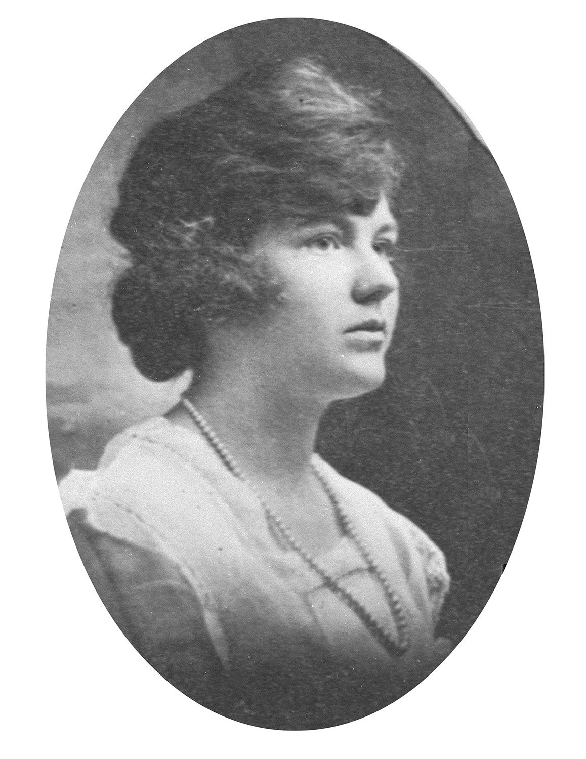 A black and white photo of a woman in a white dress and wearing a pearl necklace.