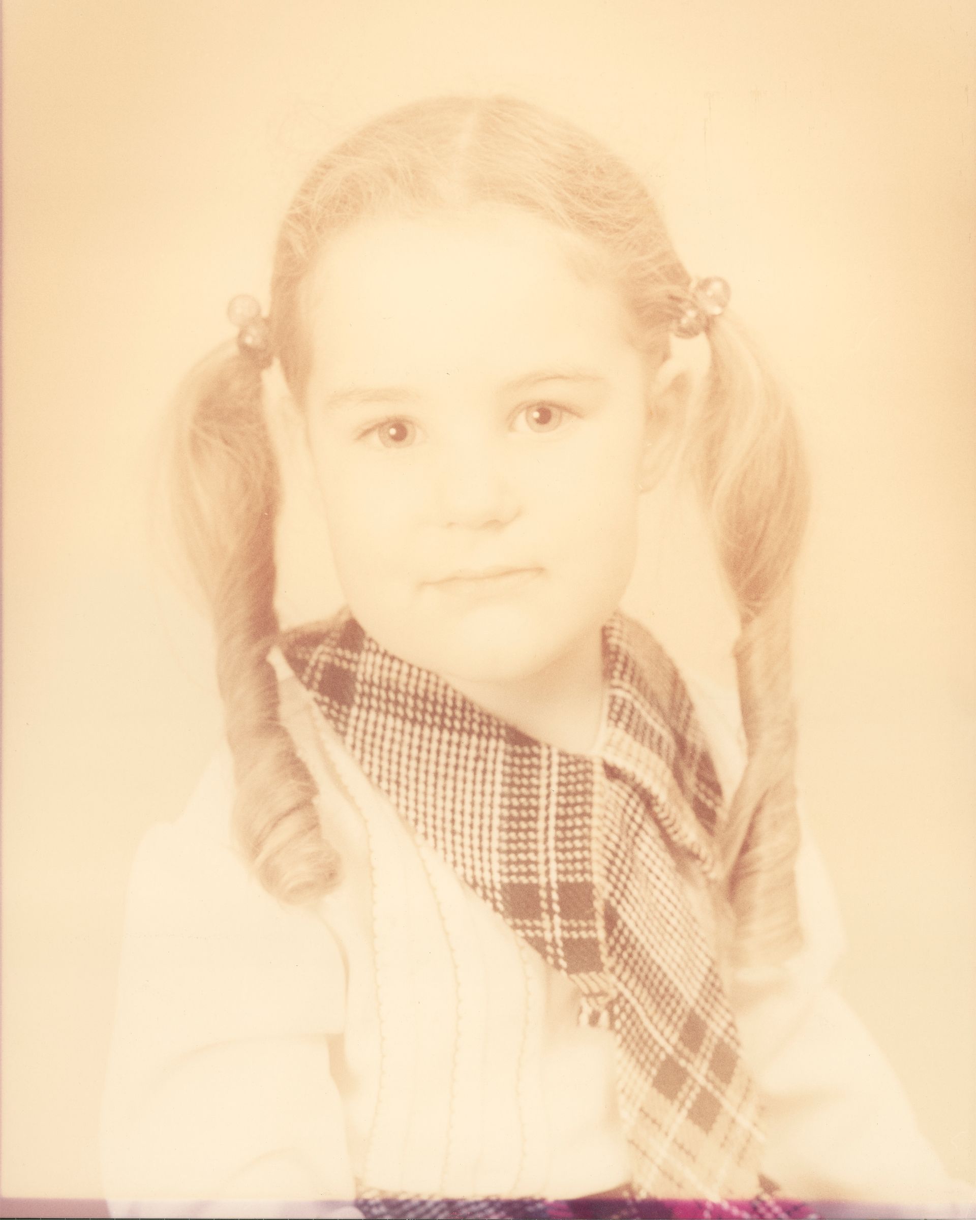 An old yellowed photo of a young girl with pigtails and wearing a plaid shirt and tie.