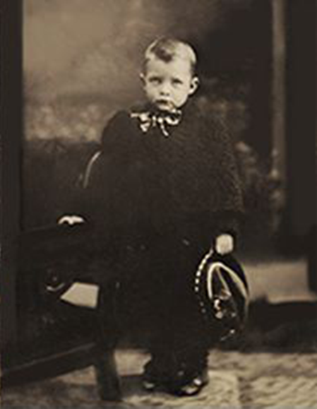 A black and white photo of a young boy holding a hat