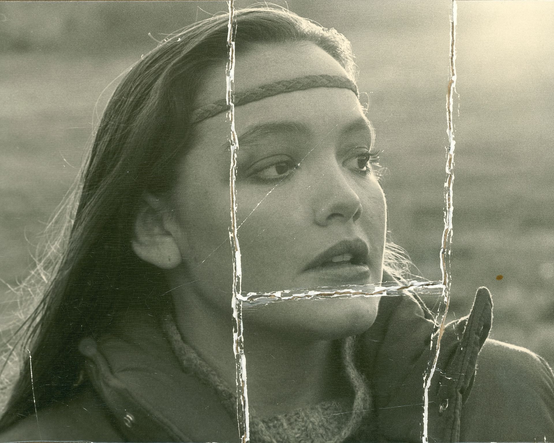 An old, damaged and yellowed black and white photo of a woman with a headband on her head.