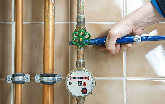 Hand turning a blue shutoff valve on a gas meter with copper pipes