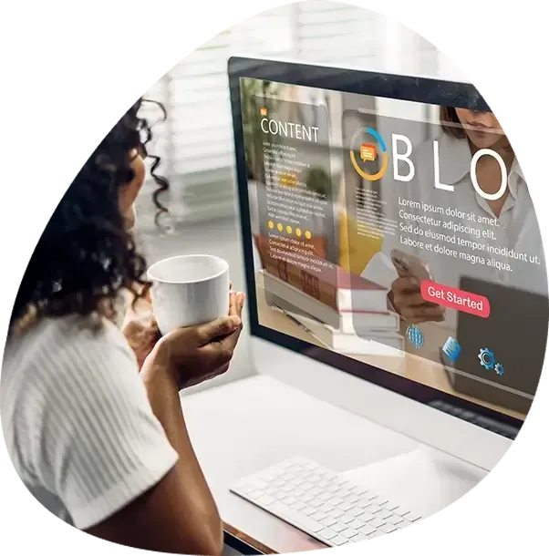 A woman is sitting in front of a computer holding a cup of coffee.