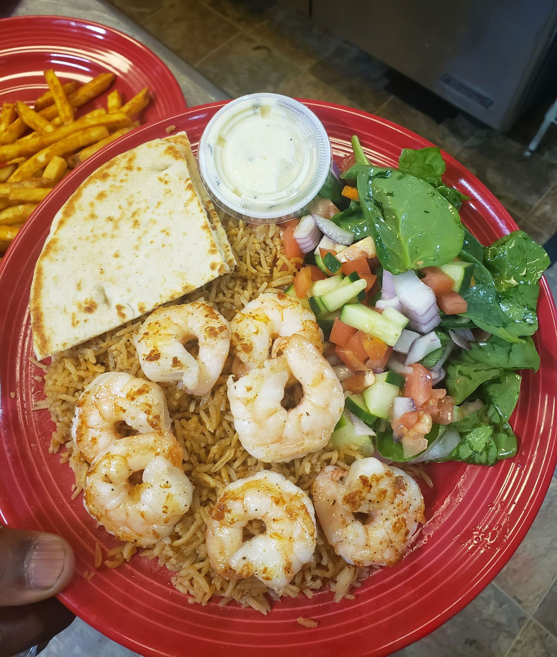 A red plate topped with shrimp , rice , salad and pita bread.