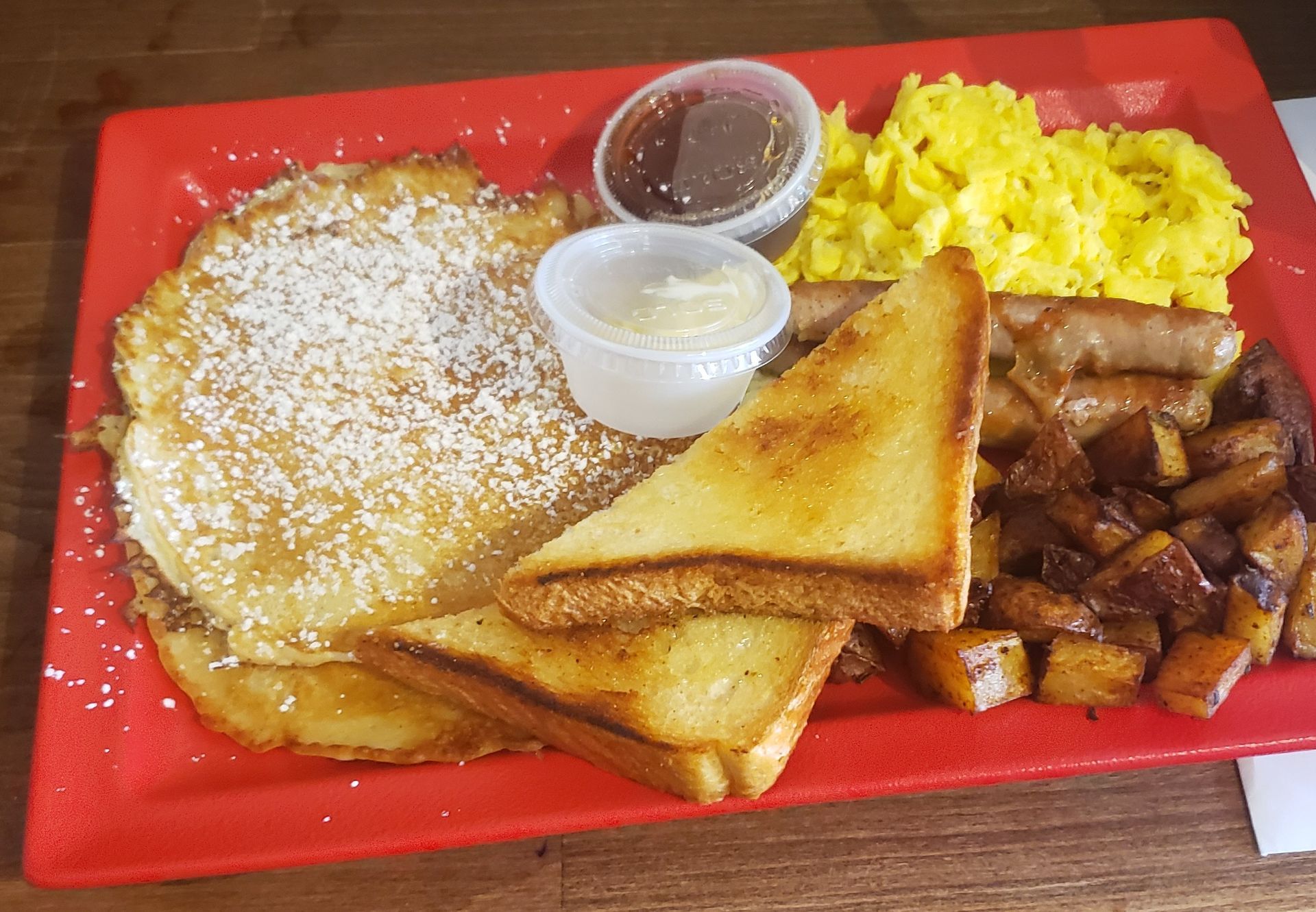 A red plate topped with pancakes , eggs , toast and sausage.